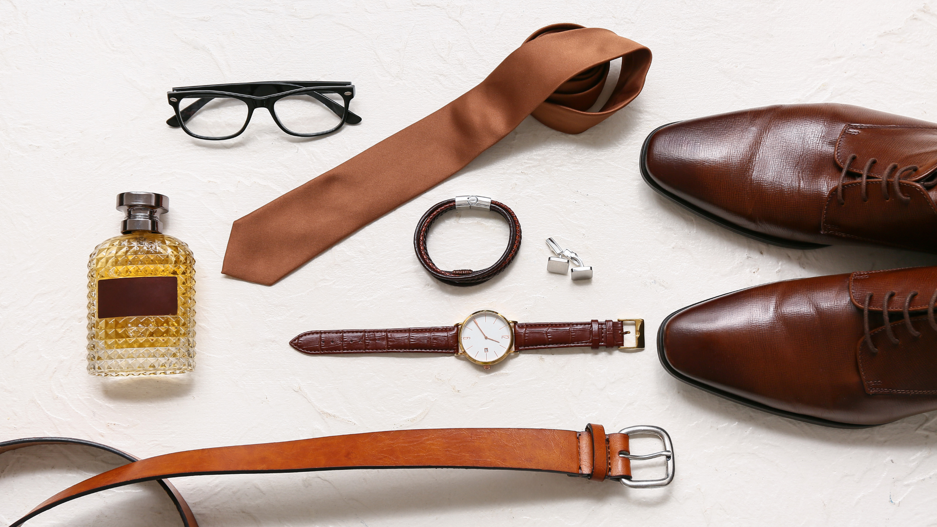 Flat lay akcesoriów: pasek, zegarek, bransoletka i okulary na neutralnym tle